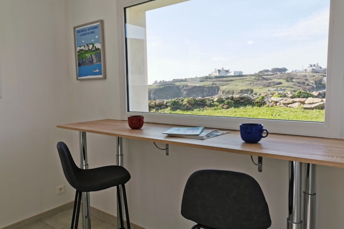 Una habitación con un ventanal grande, un escritorio, dos sillas y un cartel en la pared.