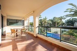 A balcony with a table and chairs, a pool, and palm trees in the background.
