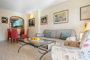 A living room with a glass coffee table, red chairs, a sofa, and artwork on the walls.