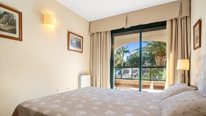 A hotel room with a bed, a window with curtains, a wall-mounted lamp, and a framed picture. - Holdiday Apartment 'Costa Linda 201' with Sea View, Pool & Wi-Fi (Hospitalet del Infante)