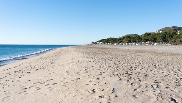 A wide sandy beach with footprints, a clear blue sky, and buildings in the background. - Holdiday Apartment 'Costa Linda 201' with Sea View, Pool & Wi-Fi (Hospitalet del Infante)