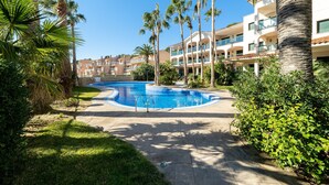 A swimming pool surrounded by palm trees and a multi-story building with balconies. - Holdiday Apartment 'Costa Linda 201' with Sea View, Pool & Wi-Fi (Hospitalet del Infante)