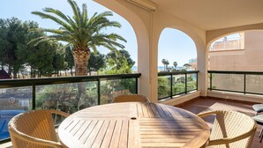 A round wooden table with wicker chairs, a palm tree, and a view of the sea. - Holdiday Apartment 'Costa Linda 201' with Sea View, Pool & Wi-Fi (Hospitalet del Infante)