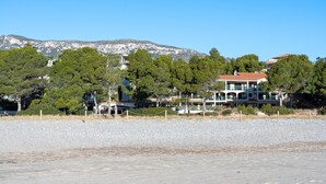A coastal property with a beach, a mountain backdrop, and a large house with multiple windows and balconies. - Holdiday Apartment 'Costa Linda 201' with Sea View, Pool & Wi-Fi (Hospitalet del Infante)