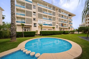 Ein Hotel mit Schwimmbad, Palmen und einem gepflegten Rasen.