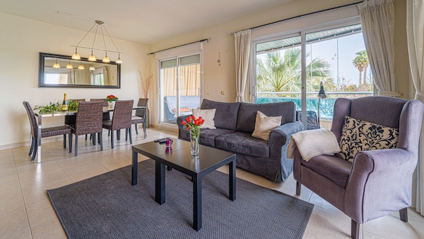 A living room with a sofa, armchair, dining table, and chairs. - Fin Albir Spaniahome Holiday Apartment with Pool, Furnished Terrace & Wi-Fi (l'Alfàs del Pi)