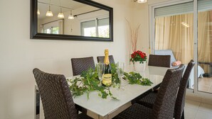 A dining table with wicker chairs, a bottle of champagne, and two glasses. - Fin Albir Spaniahome Holiday Apartment with Pool, Furnished Terrace & Wi-Fi (l'Alfàs del Pi)