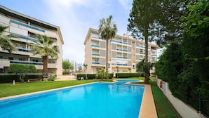 A swimming pool with a clear blue water, surrounded by greenery and a multi-story building with balconies. - Fin Albir Spaniahome Holiday Apartment with Pool, Furnished Terrace & Wi-Fi (l'Alfàs del Pi)