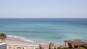 A beach view with a sailboat, a beach area with chairs, and a building with a balcony. - 'Apartment ARCE Frontline Seaview' with Pool, Balcony & Wi-Fi (Nerja)