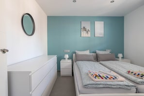 A bedroom with a bed, two bedside tables, a nightstand, a mirror, and two wall art pieces.