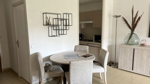 A dining area with a round table and four chairs, a kitchen in the background, and a vase with pampas grass on a cabinet.