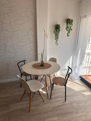 A dining area with a round table, four chairs, a vase with a plant, and a textured wall.