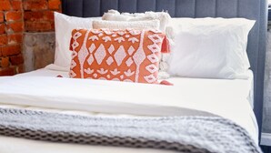 Una cama bien tendida con ropa blanca y un cojín naranja estampado.