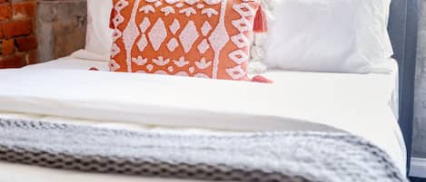 Una cama bien tendida con ropa blanca y un cojín naranja estampado.