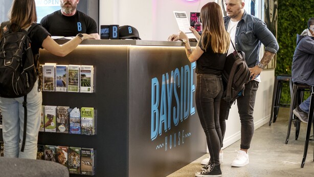 Un mostrador de recepción con un letrero que dice "BAYSIDE HOUSE" y una señal de neón arriba.
