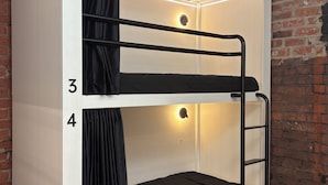 A bunk bed with numbers 3 and 4, a black curtain, and a wall with a brick pattern. - Bayside House - Hostel (St Kilda)