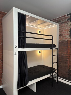 A bunk bed with numbers 3 and 4, a black curtain, and a wall with a brick pattern. - Bayside House - Hostel (St Kilda)