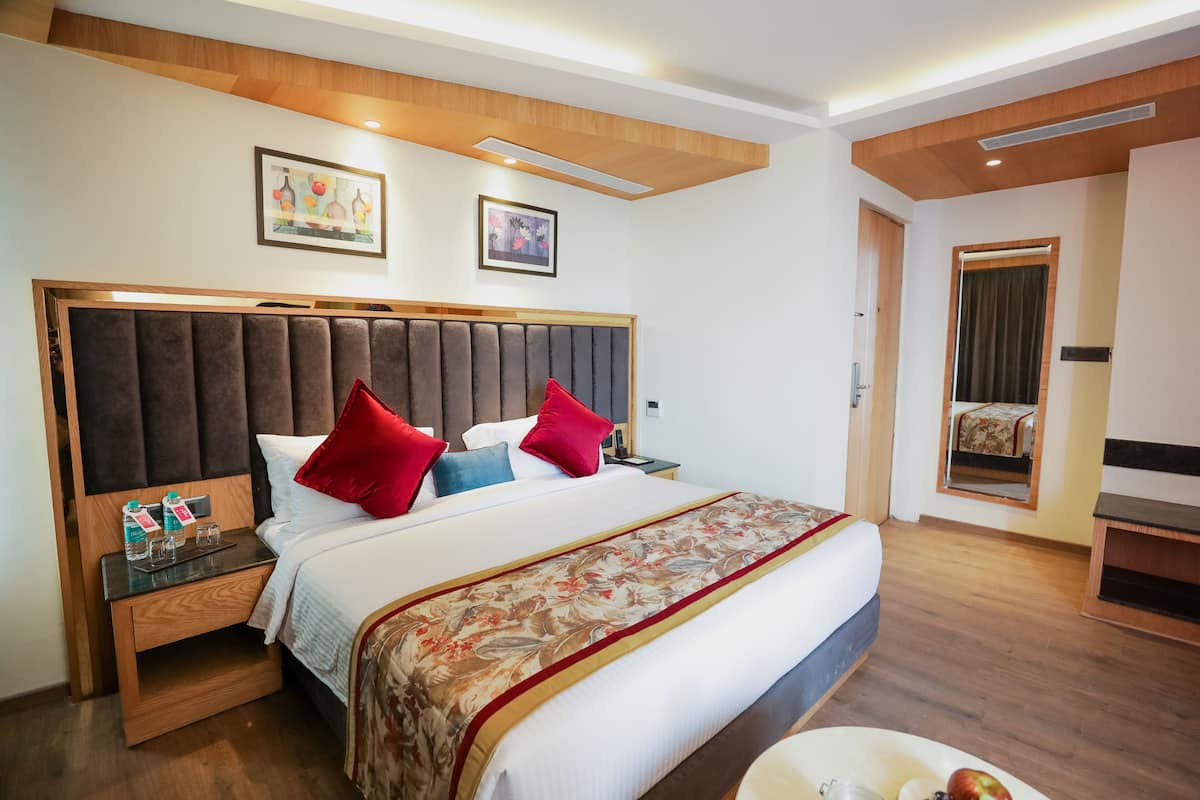 A hotel room with a large bed, wooden headboard, and a nightstand with a water bottle and glasses.