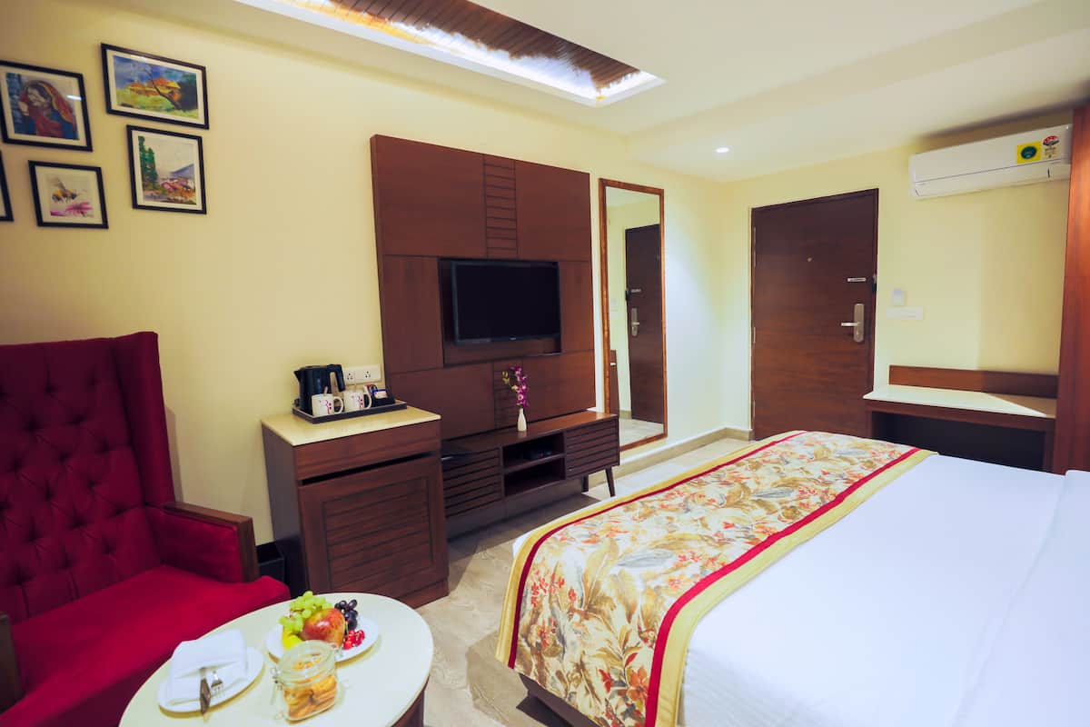 A hotel room with a large bed, a red armchair, a small table with breakfast, a TV, and a wardrobe.