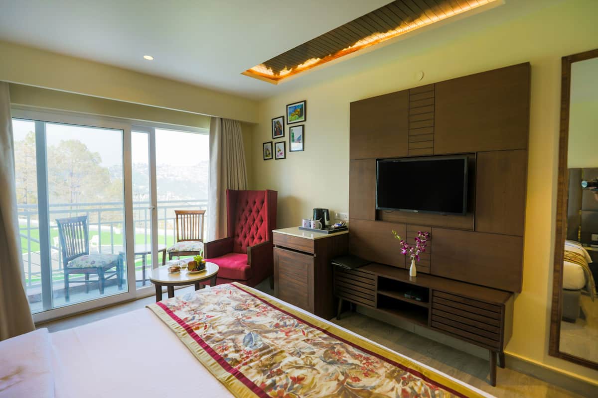 A hotel room with a large bed, a television mounted on the wall, a desk with a chair, and a balcony with a chair.