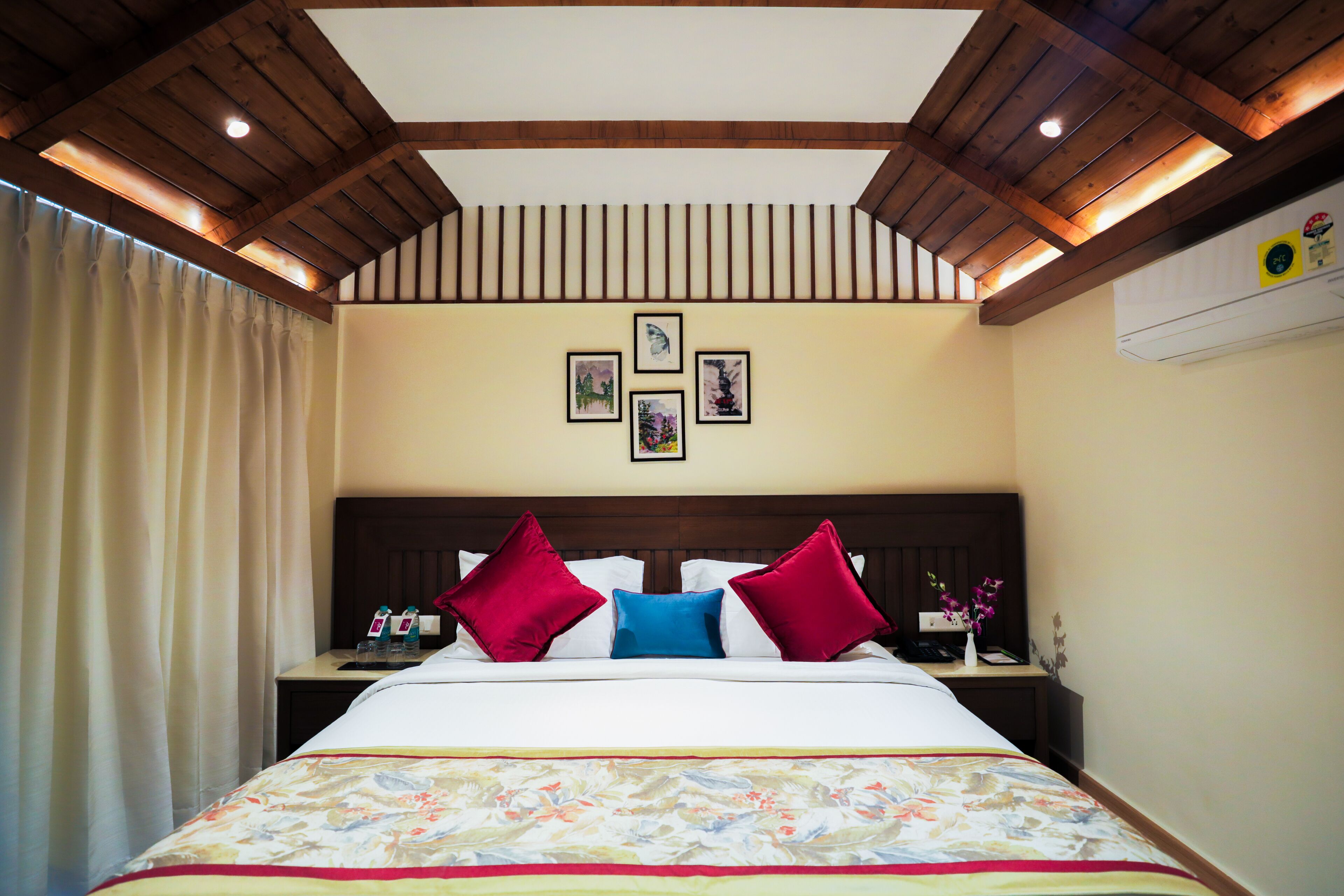 A hotel room with a large bed, wooden ceiling beams, and a wall with framed pictures.