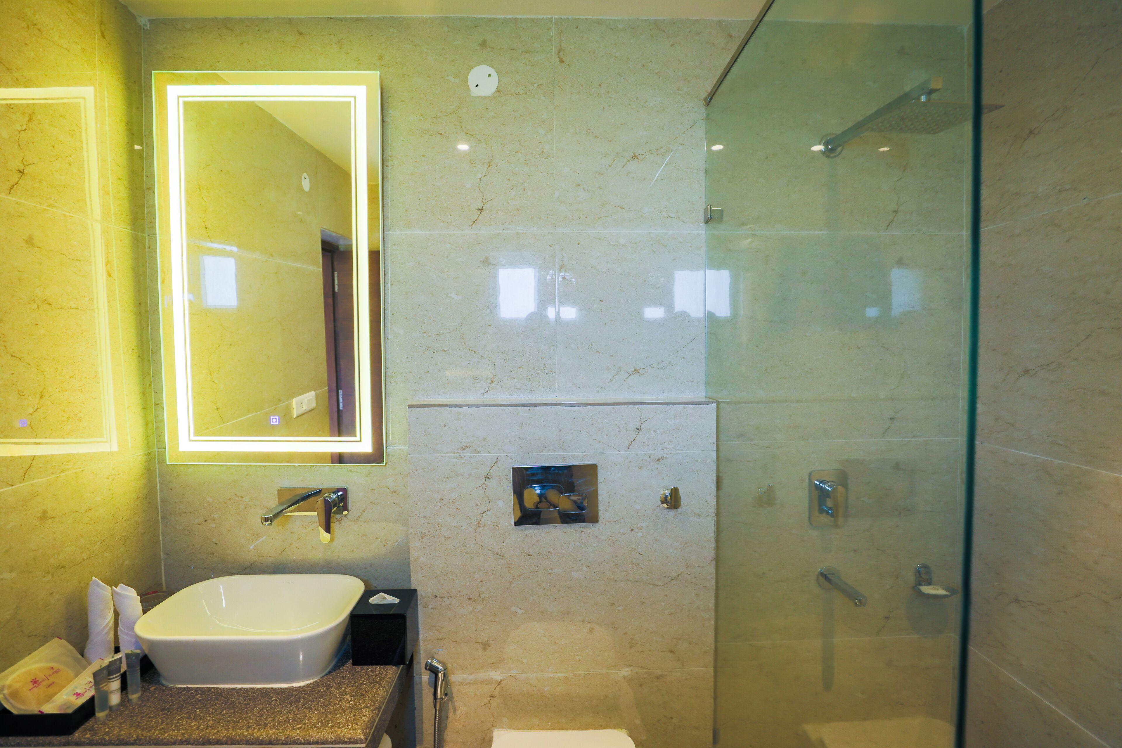 Une salle de bain moderne dotée d’une douche à parois de verre, d’un lavabo et d’un miroir dont les bords sont éclairés.
