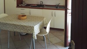 Een kleine keuken met witte kastjes, een houten tafel met een bloemig tafelkleed en een plafondventilator.
