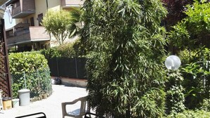Een terras buiten met een tafel en stoelen, omgeven door groen en een gebouw op de achtergrond.