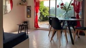 Comedor con mesa y sillas, un espejo, estantería con libros y vista a zonas verdes.