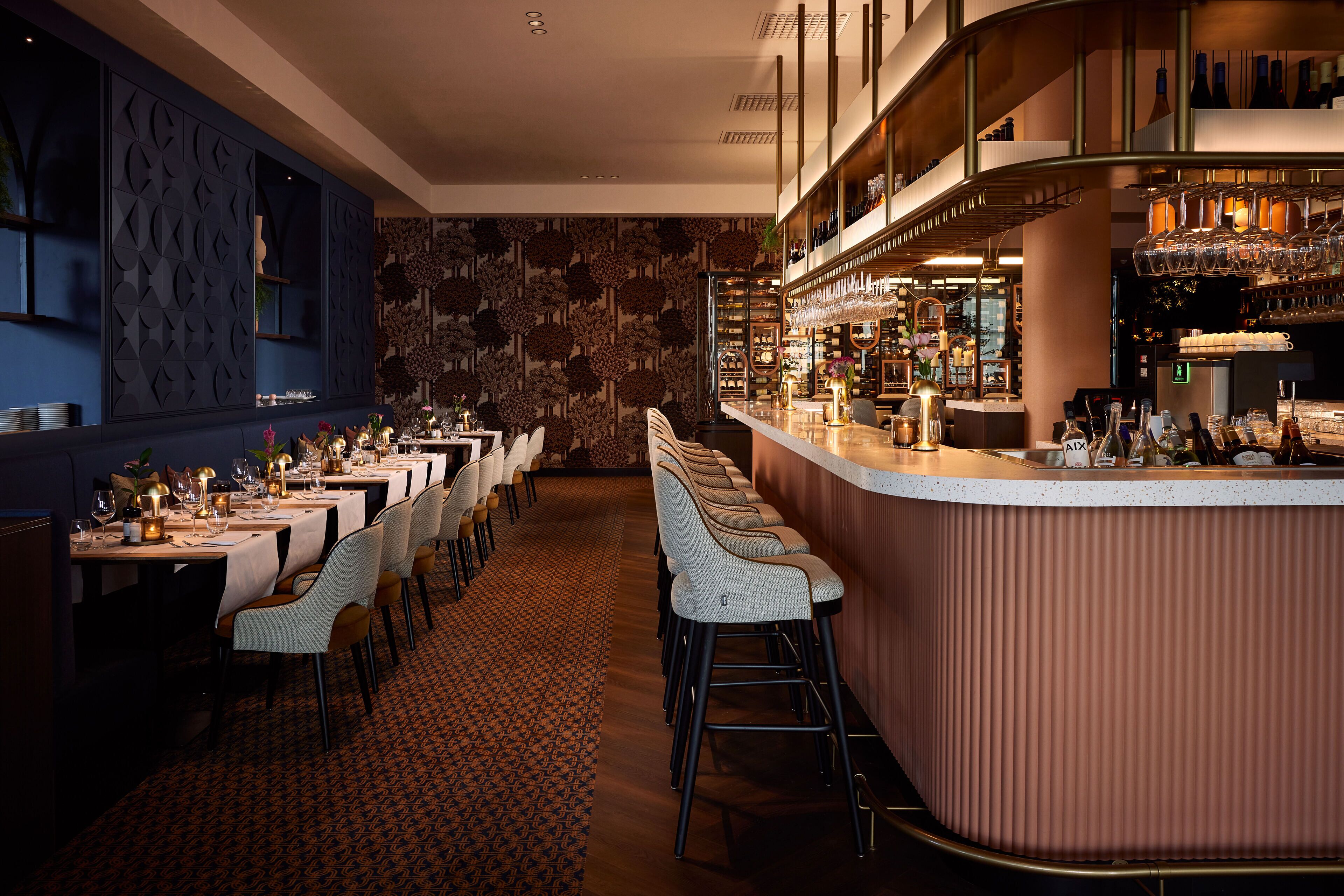 A restaurant with a long dining area, a bar with stools, and a patterned wall.