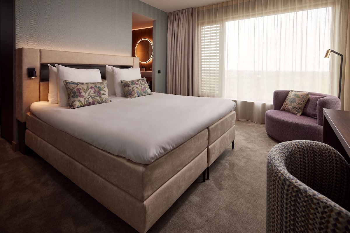 A large bed with a headboard, a bedside table, a lamp, and a chair.