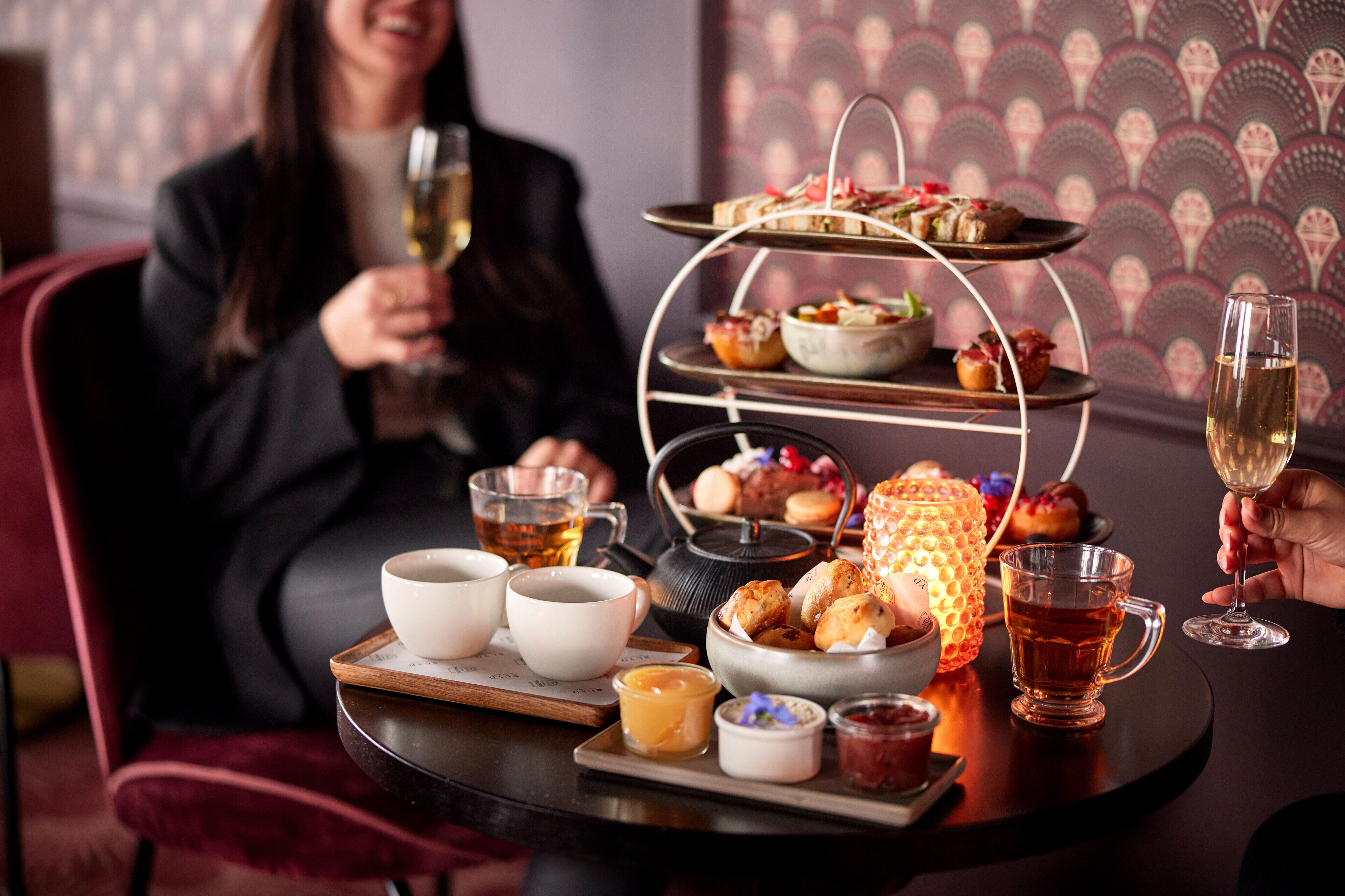 A dining table with a tiered dessert stand, tea cups, and a candle.