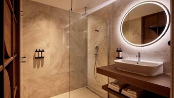Un baño moderno con ducha envuelta en vidrio, tocador con lavamanos y espejo redondo con luz.