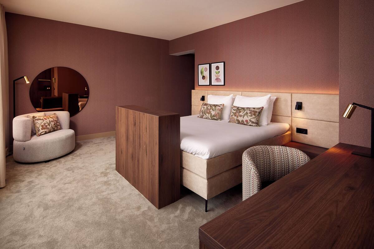 A modern bedroom with a bed, a desk, a chair, and a round mirror.