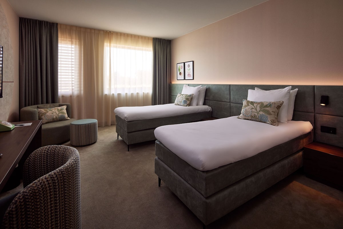 A hotel room with two beds, a desk, and a chair.
