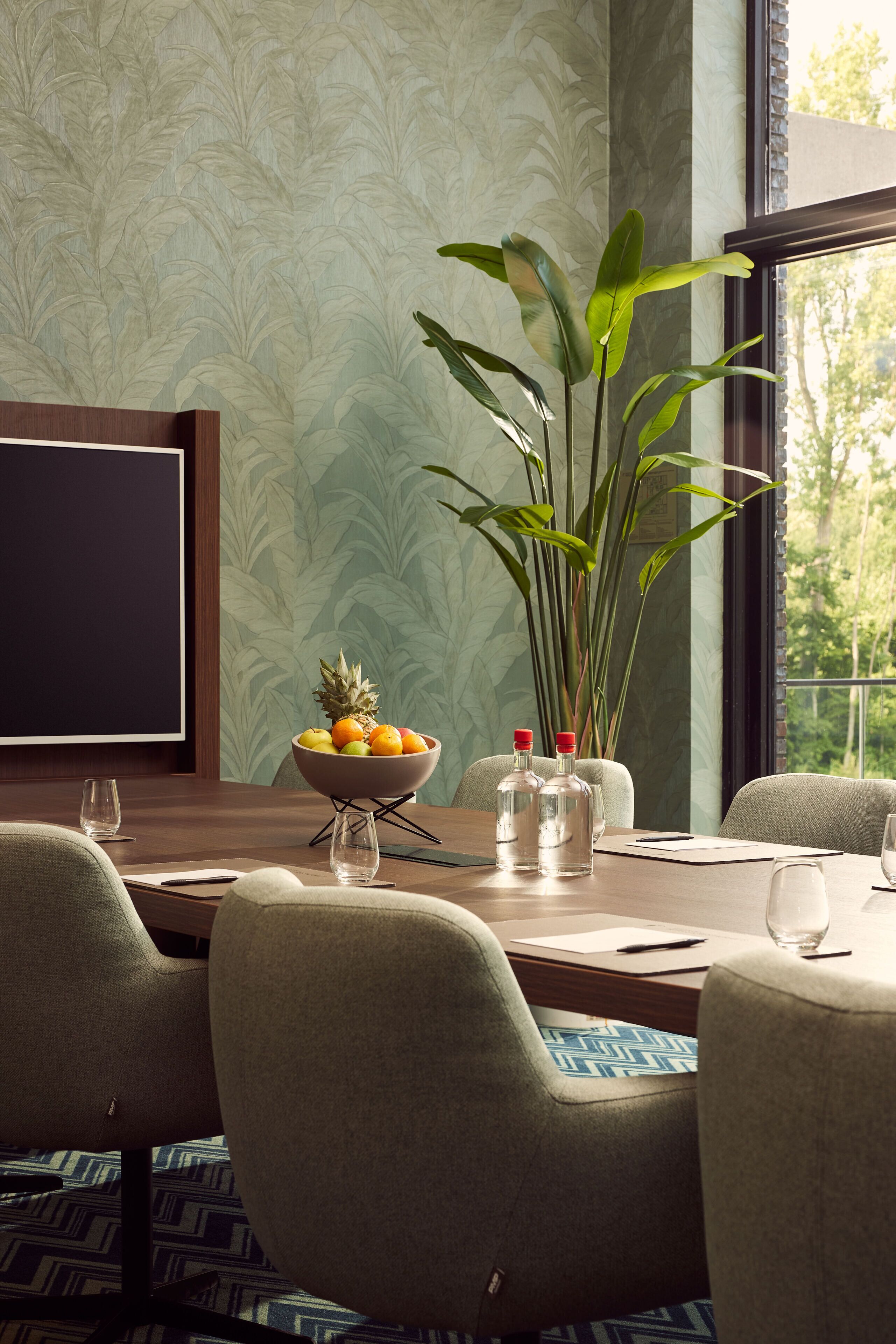 A dining area with a wooden table, chairs, a bowl of fruit, and a large plant.