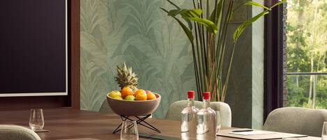 A dining area with a wooden table, chairs, a bowl of fruit, and a large plant.