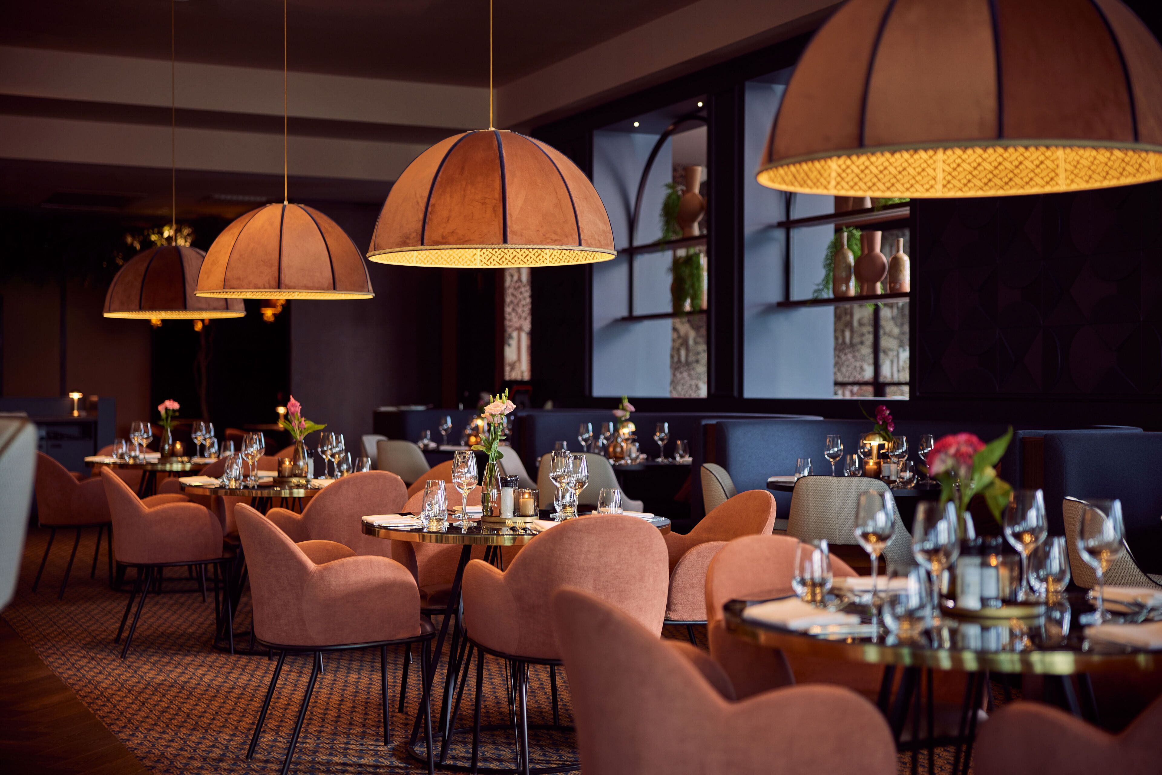 Un ristorante con diversi tavoli apparecchiati per la cena, caratterizzato da un'atmosfera accogliente con luci a sospensione e una disposizione dei posti a sedere confortevole.