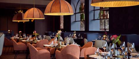 A restaurant with multiple tables set for dining, featuring a warm ambiance with pendant lighting and a cozy seating arrangement.