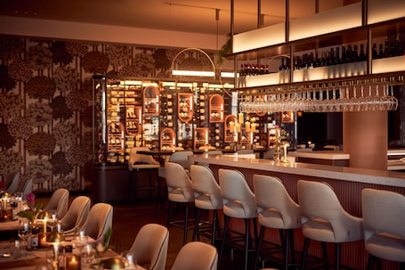 A bar area with a long counter, multiple bar stools, and a wine rack with bottles.