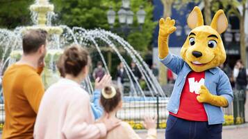 Une mascotte dans un parc avec une fontaine, et des gens en arrière-plan.