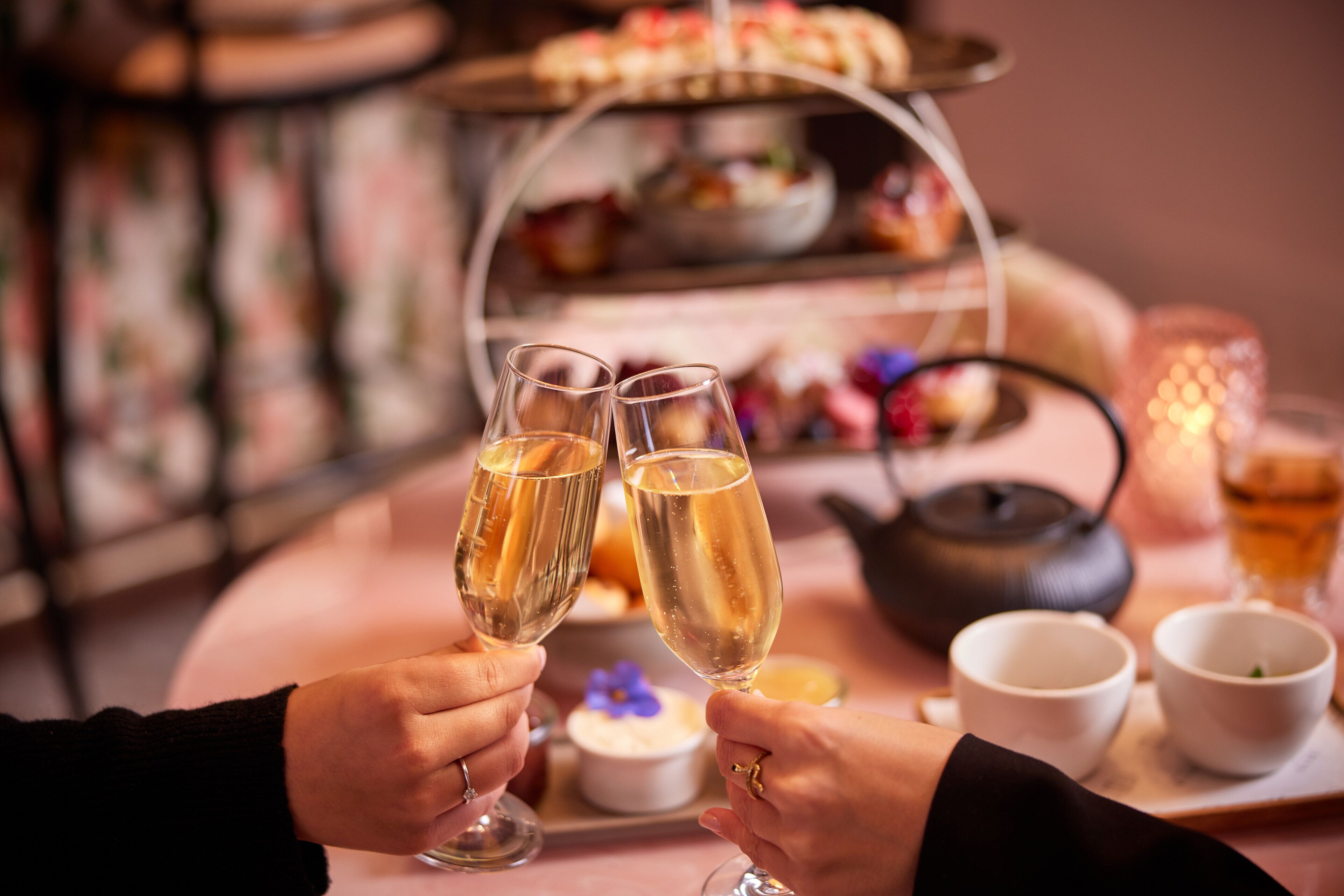 Une table avec deux coupes à champagne, une théière et, au fond, une présentation de desserts.