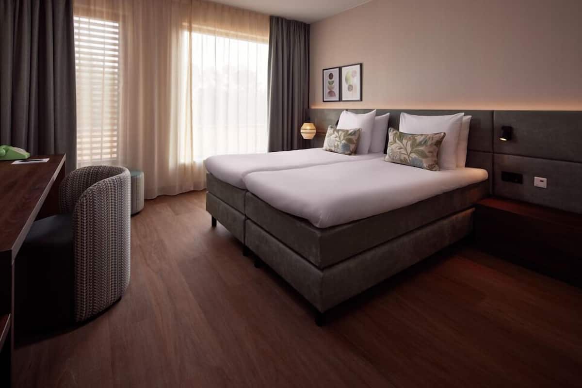 A hotel room with a double bed, a desk, a chair, and a lamp.