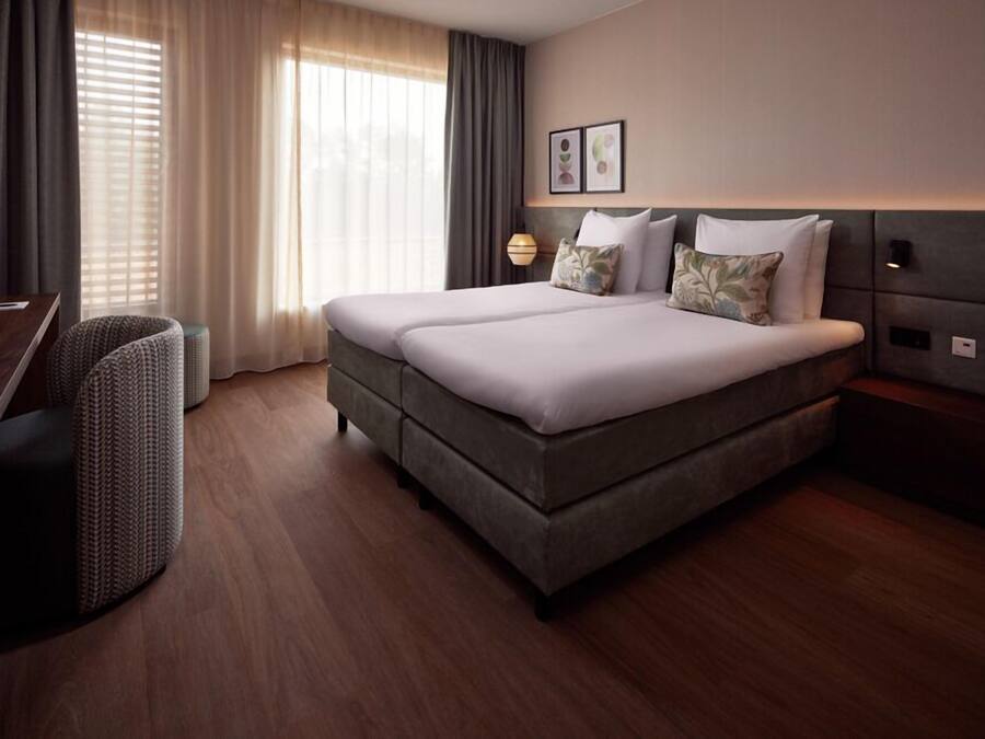 A hotel room with a double bed, a desk, a chair, and a lamp.