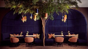A restaurant with a tree centerpiece, round tables, and cushioned seating. - Van der Valk Hotel Lelystad (Lelystad)