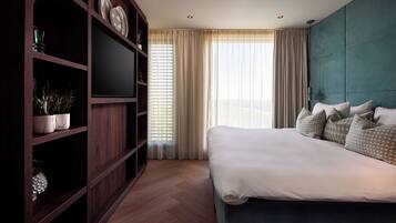 A modern hotel room with a large bed, a TV on a wooden shelf, and a view of the city through the window.