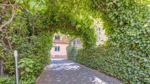 Un vialetto lastricato costeggiato da una vegetazione verdeggiante, conduce a un edificio con facciata chiara.