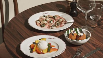 A wooden table with plates of food, a glass of wine, and cutlery.
