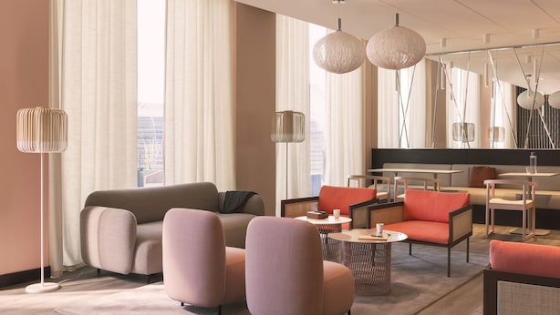 A modern hotel lobby with a sofa, armchairs, a coffee table, and a dining area. - OKKO Hotels Paris la Défense (Nanterre)