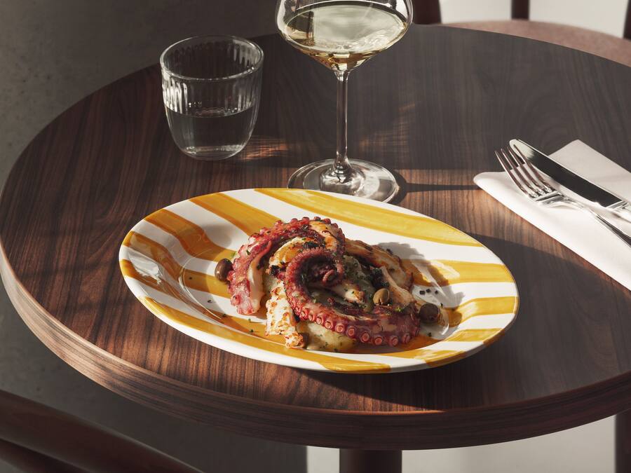 Una mesa de madera con un plato de comida, un vaso de agua y una copa de vino.